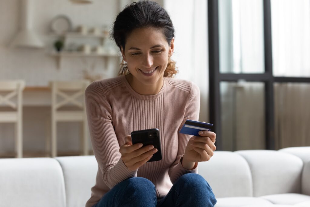 Woman Smiling Checking Her Phone And Holding Her Creditcard In The Other Hand